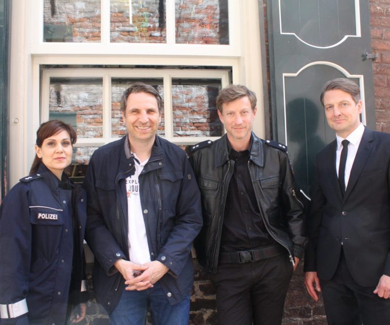 Lübbert R. Haneborger (2.v.li.) mit Sophie Dal, Maxim Mehmet und Holger Stockhaus vom Ensemble der ZDF-"Friesland"-Krimis in der Altstadt von Leer, 2023. Vier Personen, drei in ihren Filmkostümen, stehen vor einem Backsteinmauerfenster in der Altstadt von Leer.